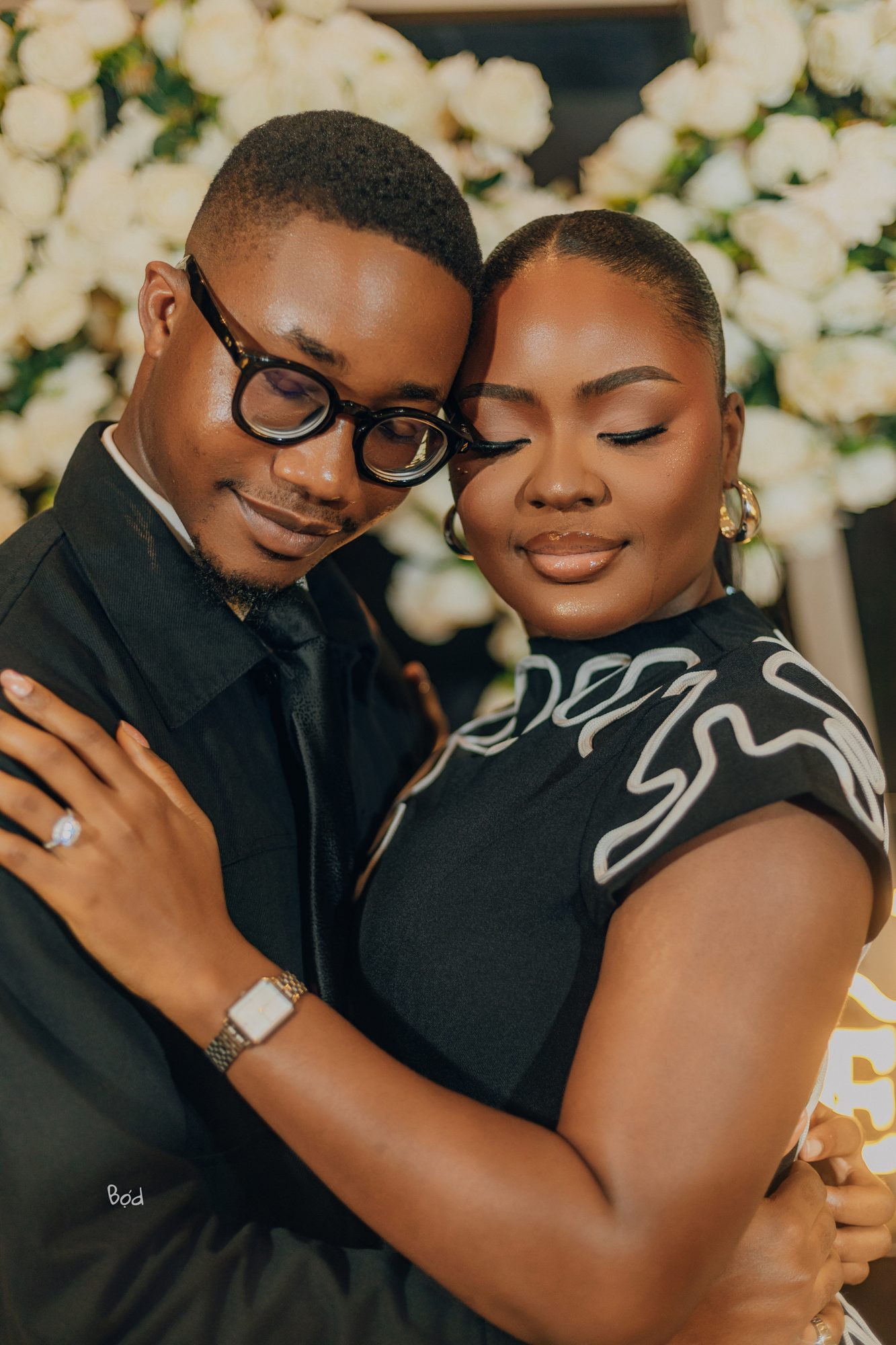 Priscilla and Kelvin embracing in front of white floral wall
